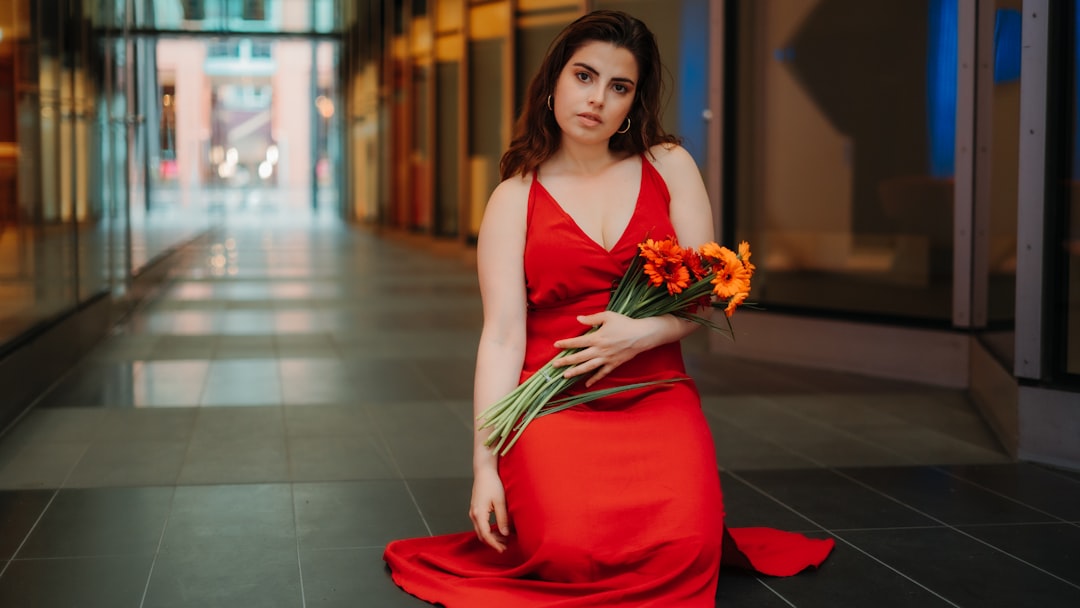 woman in red sleeveless dress standing beside red motor scooter during daytime